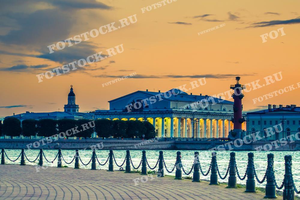 Фотография демонстрирует знаковые места Васильевского острова: Кунсткамеру, Ростральные колонны, здание Биржи в белые ночи. Набережная Невы на переднем плане с коваными оградами украшает композицию и служит прекрасным местом для прогулок. Такой снимок может быть использован в туристических путеводителях, рекламных брошюрах, а также как элемент дизайна в оформлении интерьеров или веб-страниц, посвященных Санкт-Петербургу.